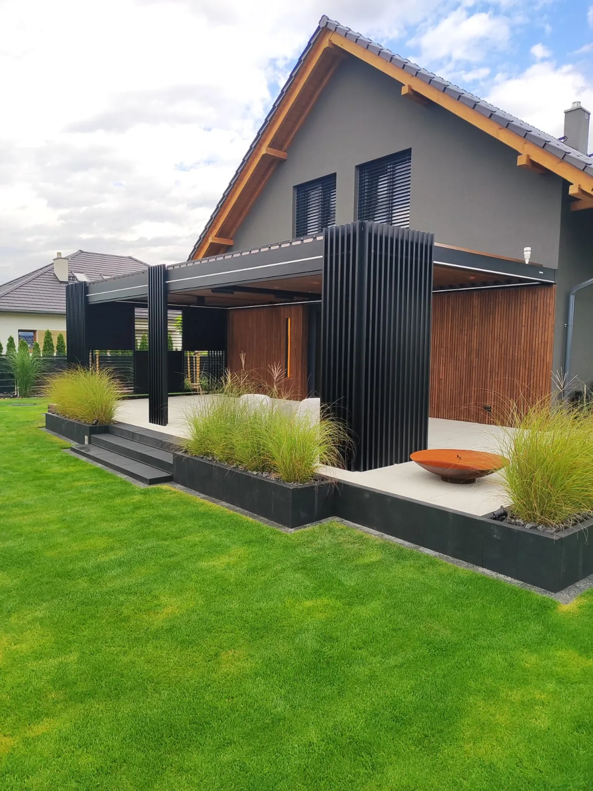 RolloMax Lamellendach Toscana mit Feuerschale und Ziergräsern am Terrassenrand